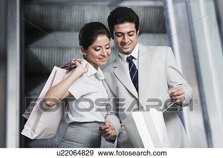Stock Photo - Business couple with shopping bags on an escalator. Fotosearch