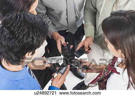 Stock Image - Business executives text messaging on mobile phones. Fotosearch