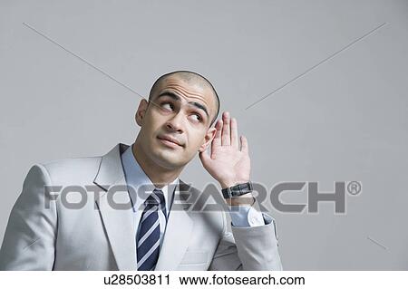 Stock Image - Businessman cupping hand to ear. Fotosearch