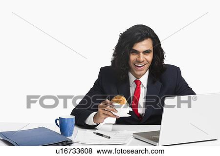 Businessman eating a burger at the desk View Large Photo Image Stock Photo - Businessman eating a burger at the desk. Fotosearch
