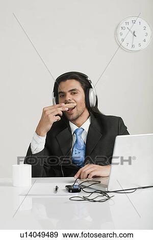 Businessman eating snacks while listening to headphones at the desk View Large Photo Image Stock Photo - Businessman eating snacks while listening to headphones at the desk. Fotosearch
