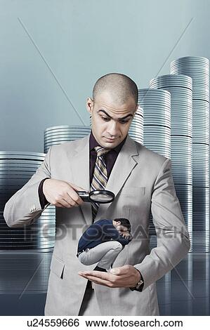 Stock Photograph - Businessman examining a small man standing on his palm through a magnifying glass. Fotosearch