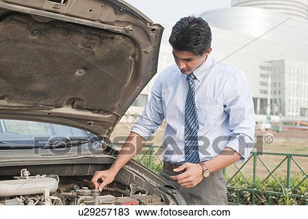 Stock Image - Businessman examining his broken down car, Gurgaon, Haryana, India. Fotosearch