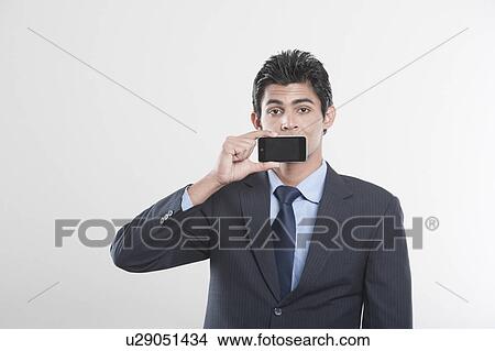 Businessman holding a mobile phone in front of his mouth View Large Photo Image Picture - Businessman holding a mobile phone in front of his mouth. Fotosearch