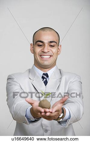 Businessman holding a sapling and smiling View Large Photo Image Stock Image - Businessman holding a sapling and smiling. Fotosearch