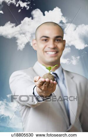 Businessman holding a sapling and smiling View Large Photo Image Stock Image - Businessman holding a sapling and smiling. Fotosearch
