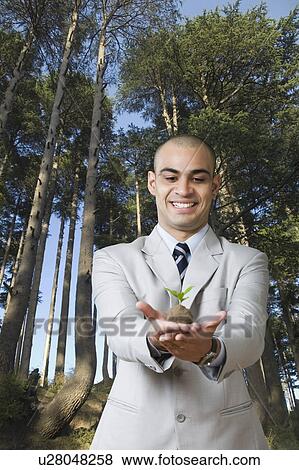 Stock Photo - Businessman holding a sapling and smiling. Fotosearch