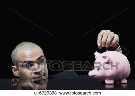 Businessman inserting a coin into a piggy bank View Large Photo Image Stock Photo - Businessman inserting a coin into a piggy bank. Fotosearch