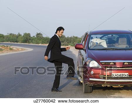 Stock Image - Businessman kicking a broken down car at the roadside. Fotosearch