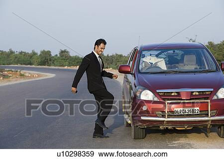 Stock Photo - Businessman kicking a broken down car at the roadside. Fotosearch