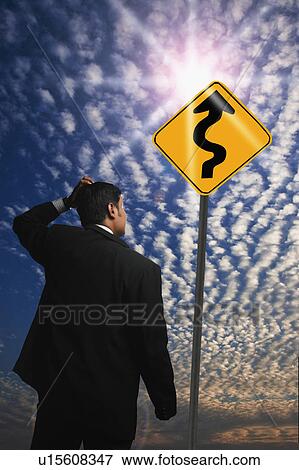 Businessman looking at a Zig Zag Road sign View Large Photo Image Stock Photo - Businessman looking at a Zig Zag Road sign. Fotosearch