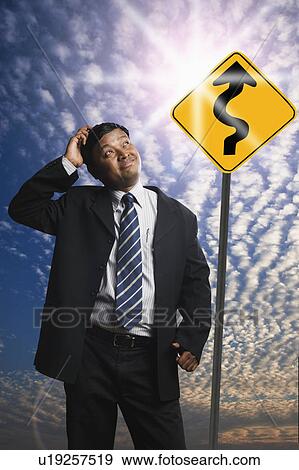 Stock Photo - Businessman looking at a Zig Zag Road sign. Fotosearch