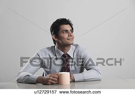 Stock Photo - Businessman lost in thoughts while drinking coffee. Fotosearch