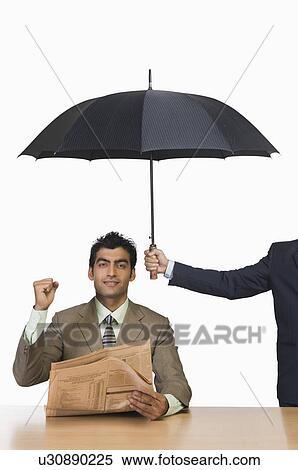 Businessman reading a newspaper under umbrella and clenching fist View Large Photo Image Stock Photography - Businessman reading a newspaper under umbrella and clenching fist. Fotosearch