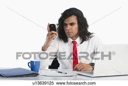 Businessman reading text message on a mobile phone at the desk View Large Photo Image Stock Photography - Businessman reading text message on a mobile phone at the desk. Fotosearch