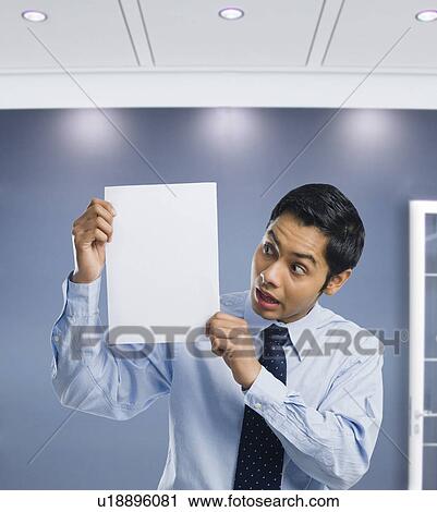Stock Image - Businessman showing a blank paper and looking surprised. Fotosearch