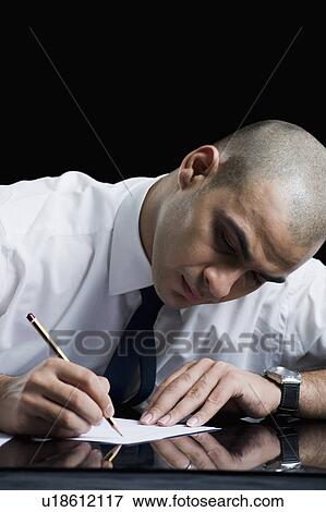 Businessman sitting at a table and writing on a sheet of paper View Large Photo Image Stock Photo - Businessman sitting at a table and writing on a sheet of paper. Fotosearch