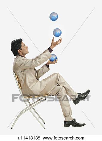 Stock Photography - Businessman sitting on a chair and juggling globes. Fotosearch