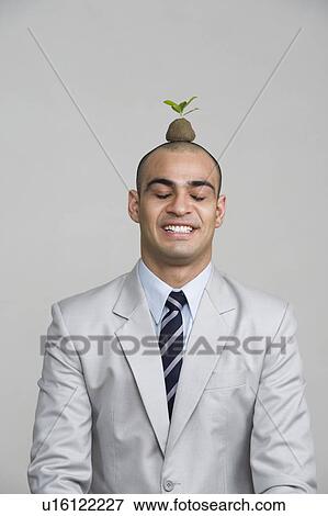 Businessman smiling with a sapling over his head View Large Photo Image Stock Photo - Businessman smiling with a sapling over his head. Fotosearch