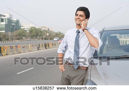 Stock Photo - Businessman standing beside a car and talking on a mobile, Gurgaon, Haryana, India. Fotosearch