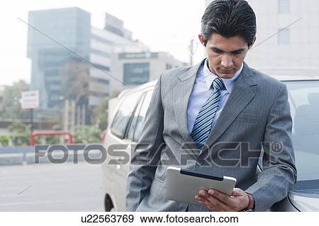 Stock Photo - Businessman standing beside a car and using a digital tablet, Gurgaon, Haryana, India. Fotosearch