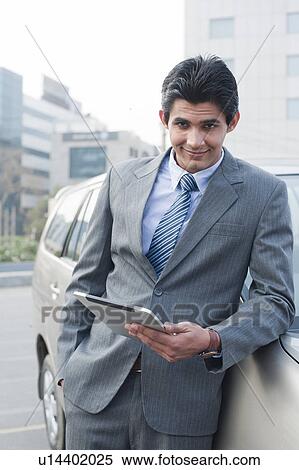 Stock Photography - Businessman standing beside a car and using a digital tablet, Gurgaon, Haryana, India. Fotosearch