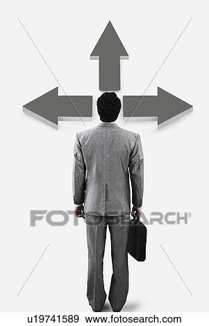 Stock Photo - Businessman standing in front of a directional sign. Fotosearch
