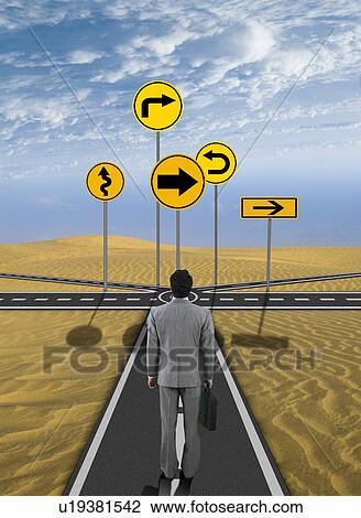 Stock Image - Businessman standing in front of road signs. Fotosearch