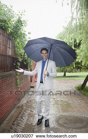 Stock Photo - Businessman standing in rain with an umbrella. Fotosearch