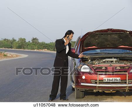 Stock Photo - Businessman standing near a broken down car and talking on a mobile phone. Fotosearch
