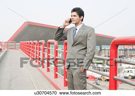 Businessman standing on a footbridge and talking on a mobile phone, Gurgaon, Haryana, India View Large Photo Image Stock Image - Businessman standing on a footbridge and talking on a mobile phone, Gurgaon, Haryana, India. Fotosearch