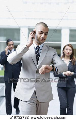 Businessman talking on a mobile phone and checking the time View Large Photo Image Stock Image - Businessman talking on a mobile phone and checking the time. Fotosearch