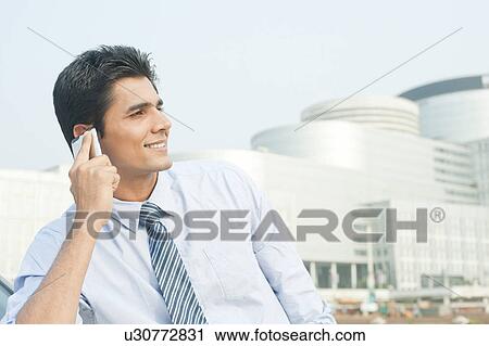 Stock Image - Businessman talking on a mobile phone outside an office building, Gurgaon, Haryana, India. Fotosearch