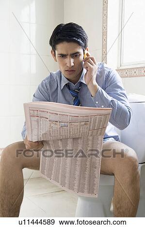 Stock Photo - Businessman talking on a mobile phone and reading a newspaper on a toilet seat. Fotosearch