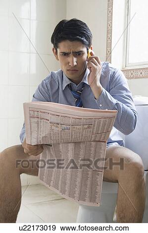 Businessman talking on a mobile phone and reading a newspaper on a toilet seat View Large Photo Image Stock Photo - Businessman talking on a mobile phone and reading a newspaper on a toilet seat. Fotosearch
