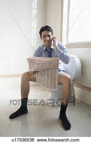 Stock Photograph - Businessman talking on a mobile phone and reading a newspaper on a toilet seat. Fotosearch