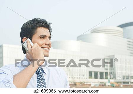 Businessman talking on a mobile phone outside an office building, Gurgaon, Haryana, India View Large Photo Image Stock Photography - Businessman talking on a mobile phone outside an office building, Gurgaon, Haryana, India. Fotosearch