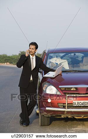 Stock Photo - Businessman talking on the phone while using a laptop. Fotosearch