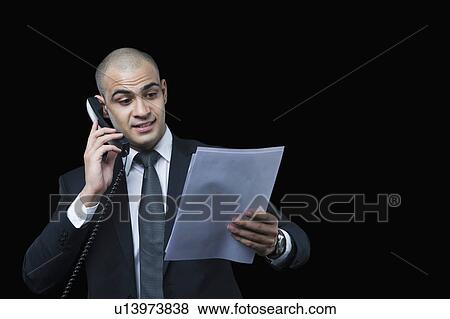 Businessman talking on the telephone and looking at a document View Large Photo Image Stock Photo - Businessman talking on the telephone and looking at a document. Fotosearch