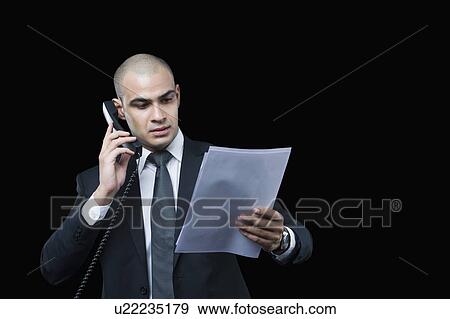 Businessman talking on the telephone and looking at a document View Large Photo Image Stock Photo - Businessman talking on the telephone and looking at a document. Fotosearch
