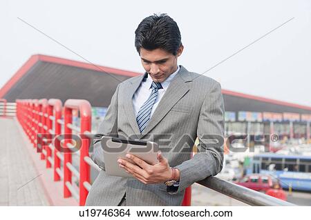 Businessman using a digital tablet at footbridge, Gurgaon, Haryana, India View Large Photo Image Picture - Businessman using a digital tablet at footbridge, Gurgaon, Haryana, India. Fotosearch