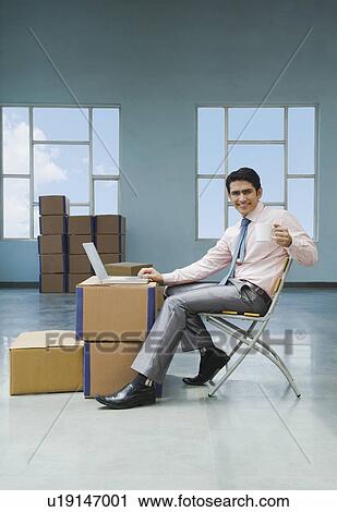 Stock Image - Businessman using a laptop and holding a cup of coffee in a warehouse. Fotosearch