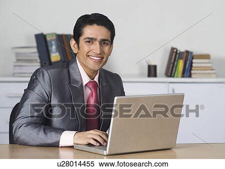 Stock Photography - Businessman using a laptop and smiling in an office. Fotosearch