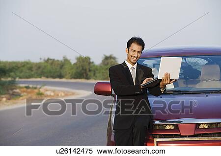 Businessman using a laptop beside a car View Large Photo Image Stock Photography - Businessman using a laptop beside a car. Fotosearch