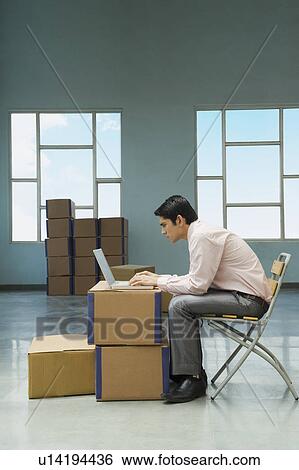 Businessman using a laptop in a warehouse with cardboard boxes View Large Photo Image Stock Photograph - Businessman using a laptop in a warehouse with cardboard boxes. Fotosearch