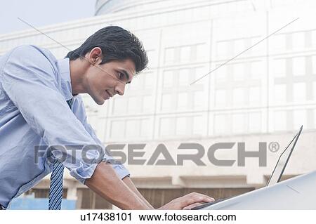 Businessman using a laptop outside an office building, Gurgaon, Haryana, India View Large Photo Image Stock Image - Businessman using a laptop outside an office building, Gurgaon, Haryana, India. Fotosearch