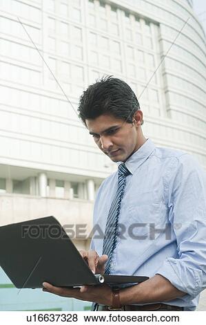 Businessman using a laptop outside an office building, Gurgaon, Haryana, India View Large Photo Image Stock Photo - Businessman using a laptop outside an office building, Gurgaon, Haryana, India. Fotosearch