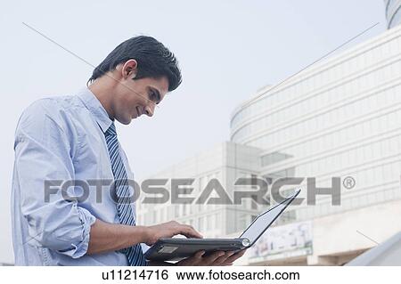 Stock Photograph - Businessman using a laptop outside an office building, Gurgaon, Haryana, India. Fotosearch