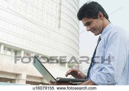 Businessman using a laptop outside an office building, Gurgaon, Haryana, India View Large Photo Image Stock Photography - Businessman using a laptop outside an office building, Gurgaon, Haryana, India. Fotosearch