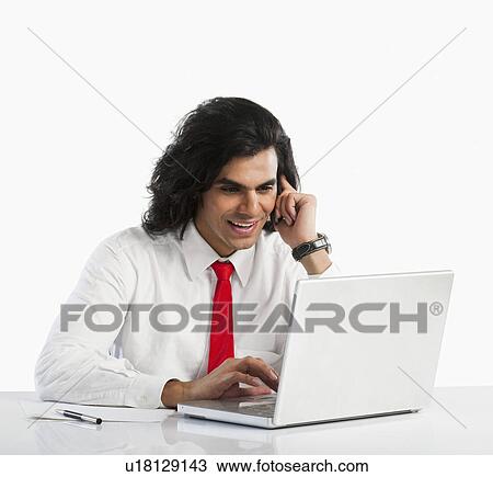 Stock Image - Businessman using a laptop while talking on a mobile phone. Fotosearch
